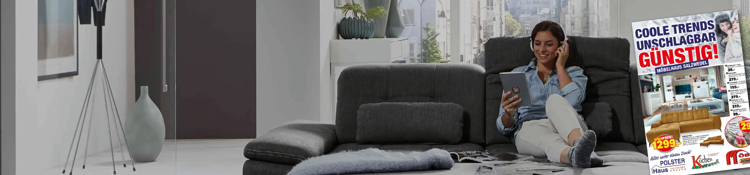 Frau sitzt entspannt auf grauem Sofa und liest die Möbelhaus Salzwedel Werbung mit günstigen Angeboten zu Sofas und Wohntrends. Moderner Wohnraum, gemütliche Atmosphäre und Fokus auf preiswerte Möbel Highlights.